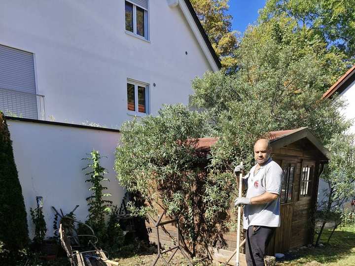 Großer Haufen Grünschnitt im Garten, dahinter Aofok Nukhailawi mit Rechen