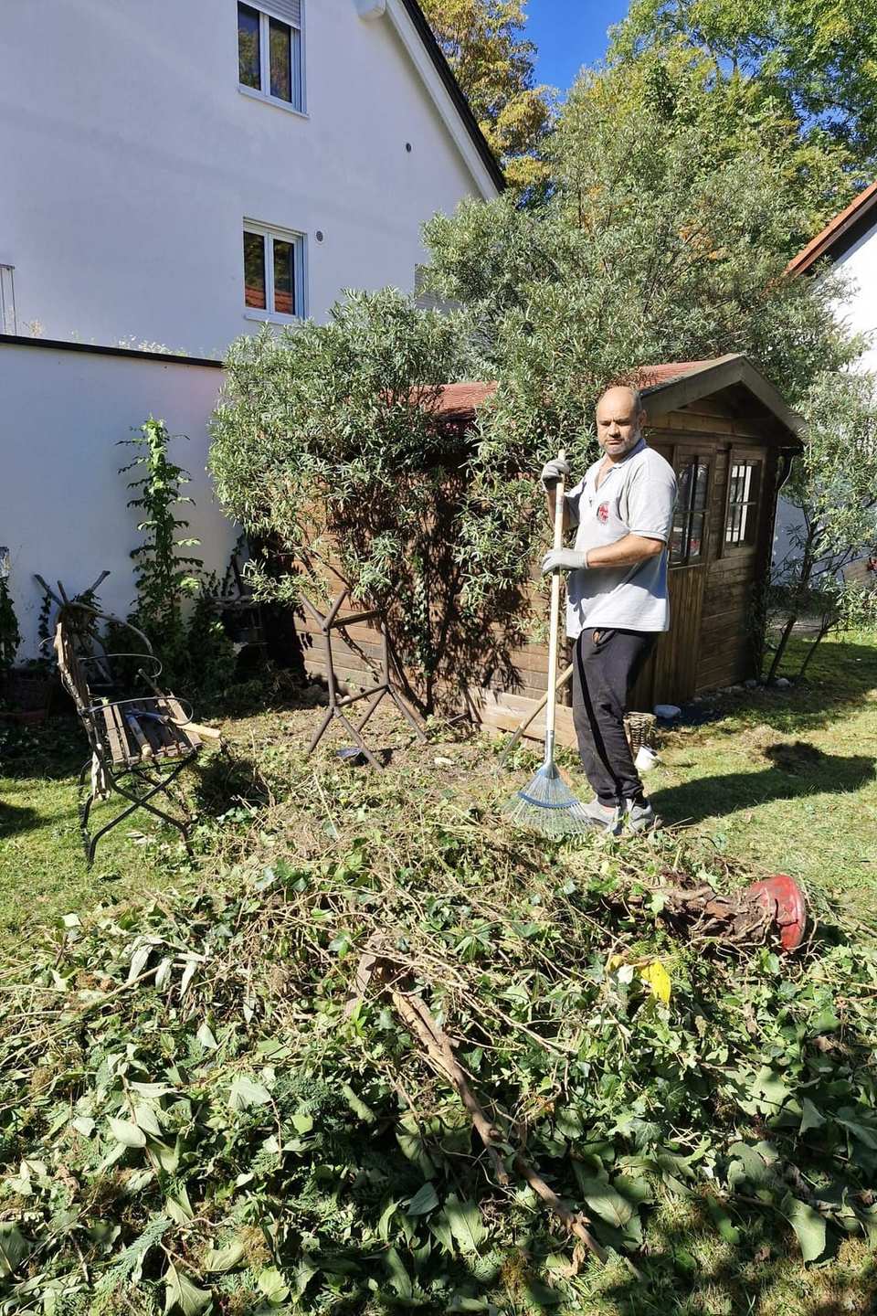 Großer Haufen Grünschnitt im Garten, dahinter Aofok Nukhailawi mit Rechen