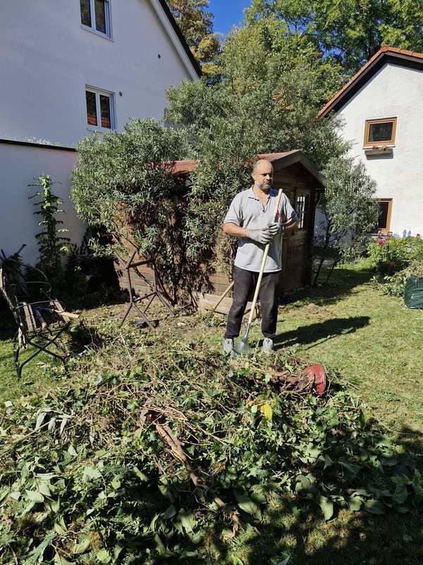 Aofok Nukhailawi mit Rechen neben aufgeschichtetem Grünschnitt