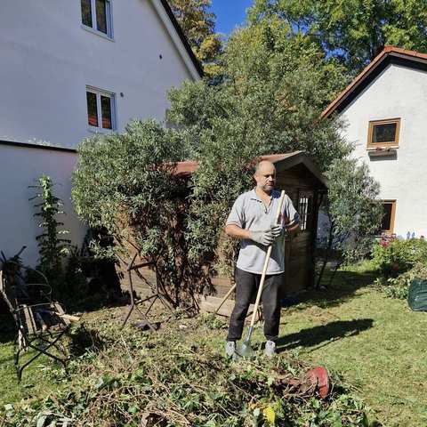 Aofok Nukhailawi mit Rechen neben aufgeschichtetem Grünschnitt
