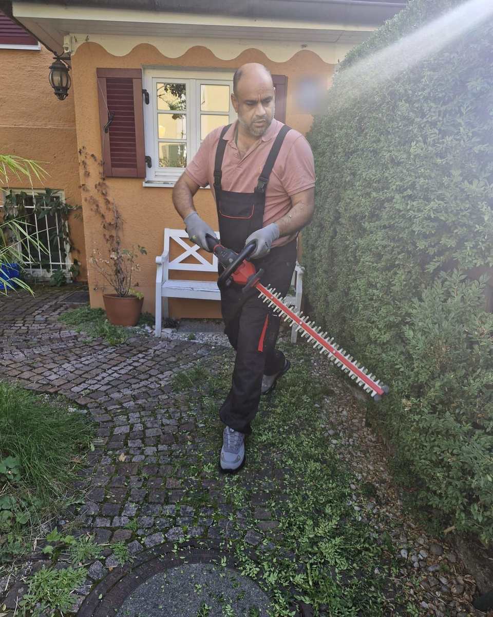 Inhaber Aofok Nukhailawi mit der Heckenschere auf einem frisch gekehrten Gartenweg